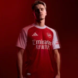 Close-up shot of the Adidas Arsenal Home Jersey 2025/26 in bold red with white sleeves and gold detailing. The embroidered Arsenal club crest sits proudly on the chest, showcasing high-quality stitching. Modern shirt pattern and lightweight fabric texture are visible, highlighting premium design and authentic match-ready style.