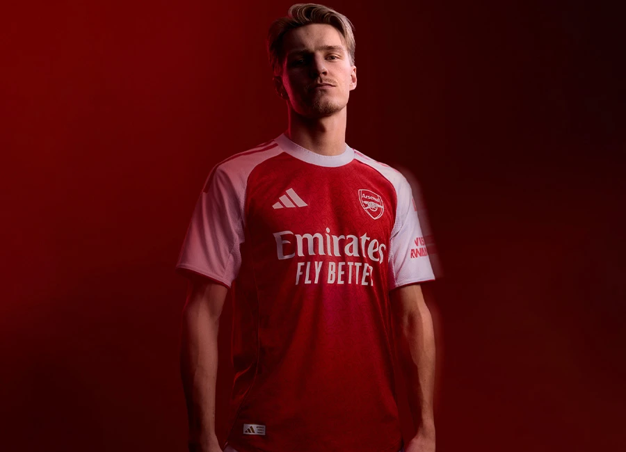 Close-up shot of the Adidas Arsenal Home Jersey 2025/26 in bold red with white sleeves and gold detailing. The embroidered Arsenal club crest sits proudly on the chest, showcasing high-quality stitching. Modern shirt pattern and lightweight fabric texture are visible, highlighting premium design and authentic match-ready style.